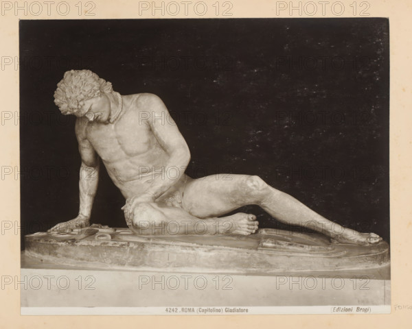 Sculpture in the Capitoline Museums in Rome, depicting the Dying Gaul, Roma (Capitolino) Gladiatore, photograph, Part of Photo album with recordings of sights and works of art in Italy., number: '4242', photographer: Edizioni Brogi, Capitoline Museums, c. 1875 - in or before 1907, Rome, paper, gelatin silver print, developing gelatin silver print, height 200 mm x width 250 mm, sculpture, deathbed, extinct, 'historical' peoples: Gauls, A photograph of a reclining marble statue of a male figure on an oval base set against a dark backdrop; the statue shows the figure leaning on one arm with his head bowed and hair in textured curls, a rope-like necklace around his neck, a muscular torso and limbs with one leg bent and the other extended, one hand resting on his knee and the other supporting his weight on the base, with visible sculpted details on the base beneath him.