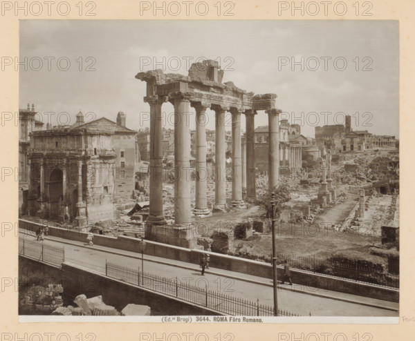 View of the Roman Forum in Rome, Roma Fôro Romano, photograph, Part of Photo album with photographs of sights and works of art in Italy., number: '3644', photographer: Edizioni Brogi, Rome, c. 1875 - in or before 1907, paper, gelatin silver print, developed gelatin silver print, height 200 mm x width 250 mm, landscape with ruins, Forum Romanum, A wide sepia-toned photograph showing a row of tall ancient stone columns with carved capitals supporting a broken entablature, surrounded by scattered ruins and low walls, with additional classical building façades and domes visible behind and beyond them; in the foreground a paved promenade bordered by a metal fence runs parallel to the ruins and shows a few pedestrians walking, while lamp posts and fragments of masonry occupy nearby ground areas.