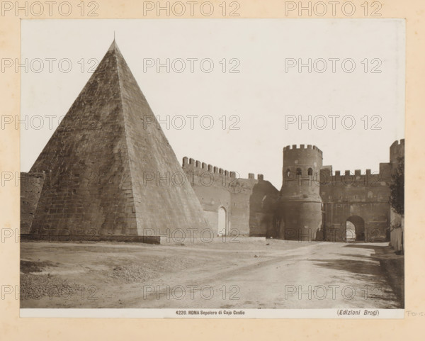 Pyramid of Cestius and the Porta San Paolo in Rome, ROMA Sepolcro di Cajo Cestio, photograph, Part of Photo album with photographs of landmarks and artworks in Italy., number: '4220', photographer: Edizioni Brogi, Rome, c. 1875 - in or before 1907, paper, gelatin silver print, height 193 mm x width 250 mm, pyramid (marking grave), gate, entrance, Porta San Paolo, Pyramid of Cestius, A large stone pyramid with a steep, textured surface occupies the left side, its apex topped by a thin vertical element, while to the right a fortified wall with battlements extends toward a circular tower featuring narrow openings and crenellations, an arched gateway beneath the tower leads into a shadowed passage and a cobbled roadway runs across the foreground with areas of compacted earth and small piles of gravel.