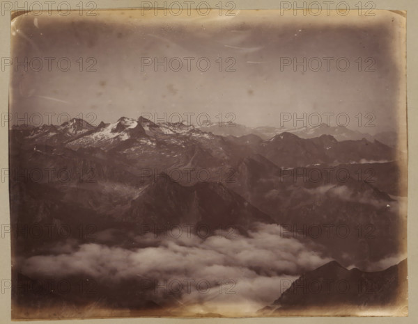 View from the Col d'Aspin, album page, photograph, This photo is part of an album., annotation: 'Vue prise de Col d'Aspin', 1880 - 1910, photographer, paper, albumen print, height 181 mm x width 233 mm, mountains, Occitanie, A sepia-toned photograph showing a panoramic view of rugged mountain peaks with patches of snow on higher summits, layered ridges receding into the distance, and a thick bank of low clouds filling the valleys below, all framed by a worn photographic border with rounded corners and slight discoloration.