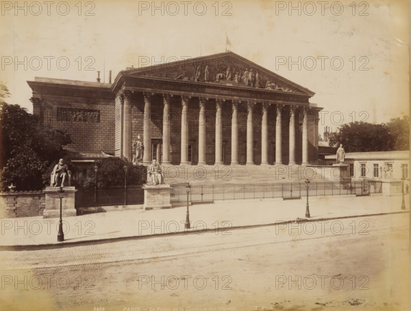 Palais Bourbon in Paris, album page, photograph, This photo is part of an album., inscription: '1488 Paris _ Le Palais de la Chambre des Députés', photographer: height 208 mm x width 272 mm, front facade, civic architecture, edifices, dwellings, Paris, Palais Bourbon, A large neoclassical stone building with a wide flight of steps leading to a portico of tall fluted columns topped by a triangular pediment with sculpted figures, flanked by blocky wings with bas-relief panels; stone statues on pedestals stand at the corners and near the stairs, and ornate street lamps line the fenced area in front; trees and shrubbery appear behind and beside the building, and a paved street and sidewalk occupy the foreground.