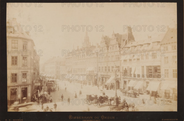 Street view in Copenhagen, Kiøbenhavn og Omegn, photograph, copyright notice: 'eneberettiget.', photographer: Edvard Valdemar Harboe, Copenhagen (city), 1862 - 1883, pasteboard, paper, albumen print, height 137 mm x width 214 mm, height 160 mm x width 236 mm, city-view, and landscape with man-made constructions, A faded sepia street scene shows multi-story buildings with pitched roofs and decorative facades lining both sides of a wide thoroughfare, awnings over many ground-floor windows and shopfronts visible along the row; a tall church spire rises above the rooftops in the distance; the street is populated with horse-drawn carriages and carts parked and moving, groups of people and scattered pedestrians, and a lamppost with ornate metalwork stands near the foreground; the image has a dark border around it and a worn, aged appearance with visible spotting and discoloration.