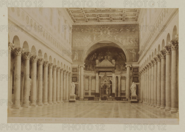 Basilica di S. Paolo furoi le mura, Interior of St. Paul outside the Walls in Rome, Italy, Roma, photograph, number: '...', photographer: Fratelli Alinari, Rome, 1852 - 1900, pasteboard, paper, albumen print, height 97 mm x width 144 mm, height 168 mm x width 223 mm, interior of church, Saint Paul Outside the Walls, A sepia-toned interior view showing a long central nave flanked by rows of tall columns with ornate capitals, arched openings above the columns on both sides, a patterned coffered ceiling, a polished floor reflecting the columns, sculpted statues on pedestals near the front, and a decorated apse with a large semicircular mosaic or painting featuring a central haloed figure and surrounding figures.