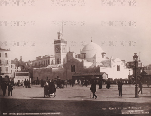 Alger, Place du Gouvernement et mosquée El-Djedid, Djama?a el Djedid mosque in Algiers, photomechanical print, address: '26 rue Bab-Azoun ALGER', number: '1001', photographer: Alexandre Leroux, Algiers, cliché maker: anonymous, c. 1875 - c. 1900, North Africa, pasteboard, paper, collotype, photoprint, height 246 mm x width 318 mm, temple, shrine, Islam, Mohammedanism, Djama?a el Djedid, A wide city square scene with many people walking and standing, some wearing long robes and head coverings, others in coats and hats, and a few animals and carts along the edges; a large mosque-like white building with domes and crenellated walls dominates the middle, accompanied by a tall clock tower with decorative panels and a flagpole, and adjacent low buildings with balconies; a prominent equestrian statue on a pedestal stands to the left, and ornamental street lamps and a small wooden structure are visible near the foreground, with long shadows cast across the open paved area under a pale sky.