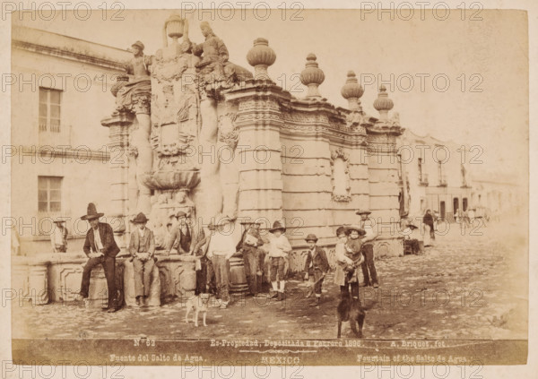 Fuente del Salto de Agua, Fountain of the Salto de Agua, View of the Salto del Agua fountain in Mexico City, Mexico, photograph, A group of men and children sit on the edge of the fountain., copyright notice: 'Es-Propriedad, Depositada 6 Febrero 1896.', number: 'N. 62', photographer: Abel Briquet, Mexico City, 1896, North America, pasteboard, paper, albumen print, height 132 mm x width 193 mm, height 160 mm x width 210 mm, ornamental fountain, Salto del Agua, A sepia-toned street scene shows an ornate stone fountain with sculpted figures, decorative urns, and carved reliefs, positioned against a building facade. Several boys and young men wearing hats and period clothing are gathered around and sitting on the fountain, some holding small objects or leaning on the stone ledge. Two dogs stand on the cobblestone street in front of the group. In the background, additional buildings with windows and balconies line the street and a few distant figures and a horse-drawn cart are visible. The ...