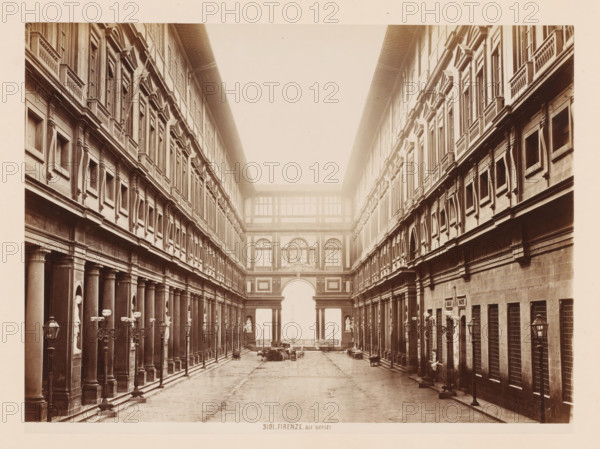 Gli Uffizi, Uffizi Gallery in Florence, Italy, Firenze, photograph, number: '3101.', address: 'GIACOMO BROGI, PHOTOGRAPHEDITORE, FIRENZE, LUNG ARNO DELLE GRAZIE 15', photographer: Giacomo Brogi, Florence, publisher: Edizioni Brogi, 1864 - 1881, Tuscany, pasteboard, paper, albumen print, height 345 mm x width 470 mm, permanent exhibition, museum, Uffizi Gallery, A long, narrow courtyard flanked by two symmetrical multi-story stone buildings with rows of tall, rectangular windows and decorative window frames; each building has a colonnaded ground level with evenly spaced columns and niches containing statues, ornate lamp posts along the walkways, and balustraded ledges beneath the upper windows; at the far end an arched gateway topped by a building section with large windows and sculptural reliefs; the paved courtyard shows scattered carts and a few indistinct objects near the central opening, and the entire scene appears in a sepia-toned photograph.