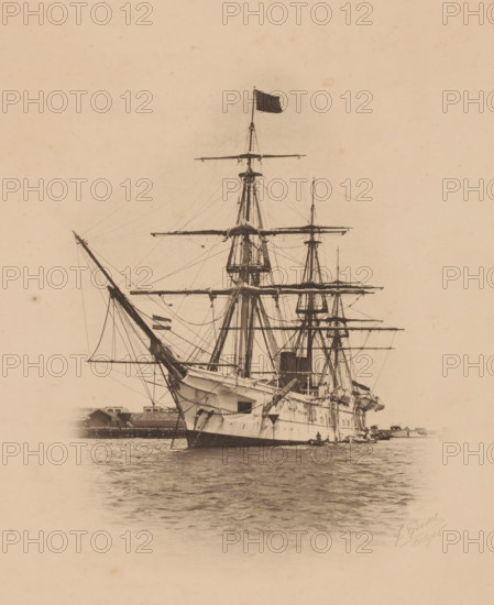 Ship at anchor, probably in Algeria (former title), Screw steamship 1st class Zr.Ms. Tromp of the Dutch Navy, photomechanical print, photographer: Jean Geiser, Algeria, cliché maker: anonymous, 1870 - 1930, North Africa, paper, pasteboard, collotype, photoprint, height 310 mm x width 244 mm, ships (in general), A large sailing ship is shown head-on on calm water, with tall masts, horizontal yards, and a dark flag flying atop the central mast; the hull is light-colored with visible anchors and rigging lines extending between masts and spars, and small boats sit alongside the ship near the stern; a low shoreline with buildings appears in the background and the image has a sepia-toned, aged appearance.