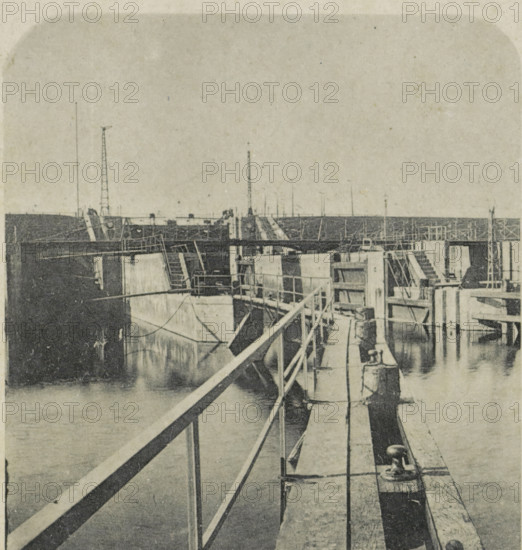 Zoutkamp - Binnenhaven, View of the Binnenhaven in Zoutkamp, photomechanical print, stereograph, number: 'No. 9.', Zoutkamp, cliché maker: anonymous, publisher: Marcus Derks de Lange, Veendam, 1900 - 1911, photographer, paper, collotype, photoprint, height 90 mm x width 170 mm, harbour, A grainy black-and-white view of a dock or pier with wooden walkways and railings extending toward the background, concrete blocks and vertical posts forming compartments alongside water, metal cleats and ropes attached to the edge, stairways and ladders leading between levels, a distant horizontal barrier or seawall across the top, and several slender poles or masts rising above the structures.