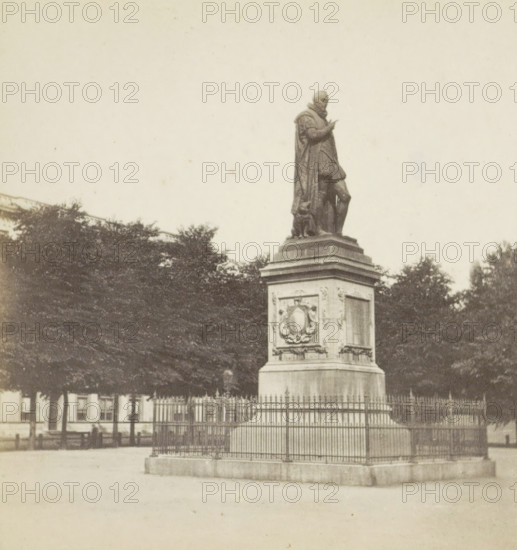 Plein The Hague, View of the statue of William of Orange by Louis Royer on the Plein in The Hague, stereograph, inscription: '...', The Hague, after sculpture by Louis Royer, 1870, Louis Royer, photographer, after sculpture by, pasteboard, paper, albumen print, height 83 mm x width 169 mm, Person, Willem I (Prince of Orange), monument, statue, Plein, A stone statue of a robed figure standing on a decorated pedestal is shown surrounded by a metal fence, the figure wearing a cloak and boots and posed with one arm raised, trees form a dark backdrop behind the monument and a building facade is visible beyond the trees.