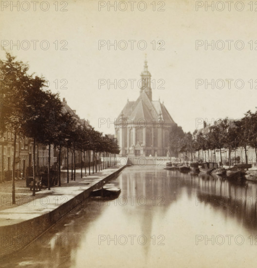 View of the Nieuwe Kerk in The Hague, seen from the Wijnhaven, The Hague, Nieuwe Kerk, stereograph, 1873 - 1890, photographer, pasteboard, paper, albumen print, albumendruk, height 85 mm x width 170 mm, parts of church exterior and annexes, A canal runs down the center of the scene with calm reflective water, flanked by tree-lined streets and rows of buildings on both sides; a large domed building with a tall ornate tower sits at the far end of the canal, visible above the trees, and small boats are moored along the canal edges; the image has a sepia tone and an aged photographic appearance.