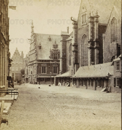 Kostershuis Haarlem, View of a street in Haarlem, stereograph, inscription: 'RBK', Haarlem, 1873 - 1890, photographer, pasteboard, paper, albumen print, height 85 mm x width 169 mm, urban housing, street, A sepia-toned street scene showing a wide cobbled road flanked by tall ornate stone buildings with pointed roofs and large arched windows, a long covered colonnade along one side with wooden posts and a sloped roof, decorative facades with sculpted details and pinnacles, a horse-drawn carriage in the distance near the buildings, benches and steps along the near sidewalk, and small bollards lining the street.