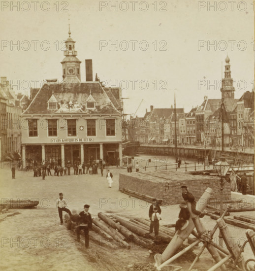 Middelburg, View of city coffee house De Beurs in Vlissingen, stereograph, inscription: 'MB', inscription: 'Rotterdam', inscription: '25', 1861 - 1870, photographer, pasteboard, paper, albumen print, height 88 mm x width 178 mm, restaurant, square, circus, building activities, Flushing, Beurs (Vlissingen), A waterfront scene showing a large multi-story building with a steep tiled roof topped by a clock tower and decorative sculptures above its upper windows, a colonnaded ground floor with people gathered in front, a row of narrow buildings extending along the canal to the right with a taller ornate tower rising among them, several masts and rigging of moored boats along the water, stacked wooden logs and large timbers on the quay with people sitting and standing on and around them, a brick platform at the quay edge, and scattered figures walking or standing across the open cobbled area in front of the quay.