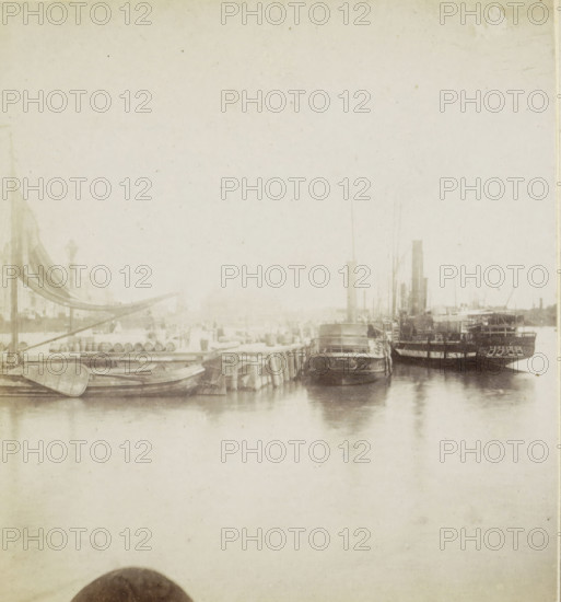 De Oosterkade., Quai dit Oosterkade., Der Kai Oosterkade., Guay called Oosterkade, View of the Oosterkade in Rotterdam, Rotterdam, stereograph, 1857 - 1863, photographer, pasteboard, paper, albumen print, albumendruk, height 88 mm x width 175 mm, ships (in general), quay, A faded sepia-toned waterfront scene showing several moored boats and ships along a wooden dock, with small rowboats in the foreground and larger steam or sailing vessels closer to the right, masts and funnels rising above the decks, reflections visible in the calm water, a series of barrels and dockside structures along the left side, and a light, grainy sky filling the upper area.