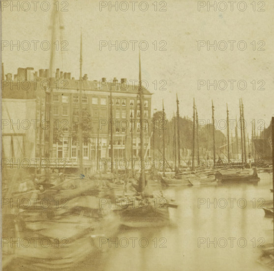 Vue prize a Rotterdam, View of the Old Harbor in Rotterdam, Hollande, stereograph, inscription: 'Rotterdam', inscription: 'Nieuwe Haven', number: 'N. 36.', photographer: Charles-Henri Plaut (possibly), Rotterdam, publisher: attributed to Alexis Gaudin et Frère, Paris, 1858, Attributed to, pasteboard, paper, albumen print, albumendruk, height 84 mm x width 167 mm, harbour, city-view in general, 'veduta', ships (in general), Oudehaven, A faded sepia view of a waterfront scene showing tall slender masts rising from moored boats in the foreground and midground, with a row of multi-story buildings behind the boats; the buildings have multiple windows and a pitched roof with chimneys, and trees are visible between and behind some masts, while the water reflects blurred shapes of the boats and masts.