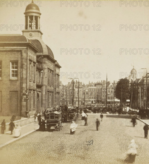 View of the Rotterdam Stock Exchange building, stereograph, inscription: '1.50', inscription: 'No. 74', Rotterdam, 1861 - 1870, photographer, pasteboard, paper, albumen print, height 86 mm x width 174 mm, street, Exchange, Bourse, Beurs (1736-1940), A sepia-toned street scene with a large stone building on the left featuring tall windows and a rounded dome tower, a cobbled road running down the center lined with horse-drawn carriages and wagons, blurred pedestrians in period clothing walking along the street and sidewalks, rows of narrow multi-story buildings and rooftops visible in the distance, tall masts from docked boats rising above the waterfront on the right, and a tree-lined area near the right edge with a domed structure visible behind it.