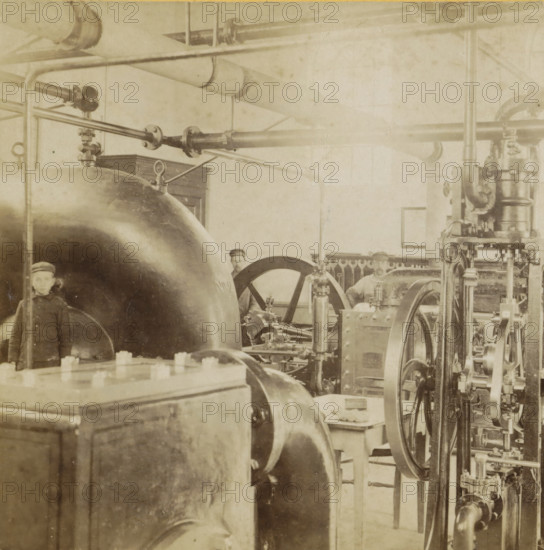 Interior of a water machine, A machine room, Geographical sculpture gallery, collected by MJ Broekhuijsen, headmaster of a school in Amsterdam, Collection E, stereograph, inscription: 'RBK', number: '5.', inscription: 'Interior of a water machine.', Netherlands, publisher: Merkelbach & Co., Amsterdam, compiler (person in literature): Martien Johan Broekhuijsen, 1900 - 1902, photographer, compiler (person in literature), pasteboard, paper, albumen print, height 86 mm x width 176 mm, machine driven by water, A sepia-toned industrial interior showing large curved metal tanks and cylindrical machinery with visible bolts and flanges, an array of pipes and horizontal rods running across the upper area, several wheels and flywheels with spokes, vertical rods and mechanical linkages, a wooden cabinet partially visible against the wall, a framed rectangle on the wall, and two partially visible figures wearing caps standing among the equipment.
