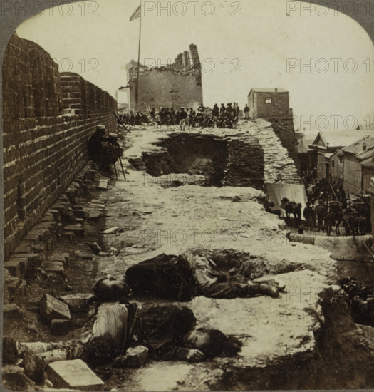 Victims of the Battle at Tientsin in China, stereograph, inscription: 'We are just inside the southern wall of the, native city' at Tientsin. July 14, 1900. It has, been fiercely besieged by, ', number: '59', copyright notice: 'Copyright 1901 by Underwood & Underwood.', inscription: 'SUN SCULPTURE, UU, TRADEMARK, Works and Studios, Arlington, NJ Westwood, NJ Washington, DC', title: 'Chinese people Paid War's Penalty, Tientsin, China.', Tianjin, publisher: Underwood and Underwood, New York (city) (possibly), 1900-07-14, photographer, North America, pasteboard, paper, albumen print, height 88 mm x width 178 mm, death of human being, Boxer Rebellion, A narrow elevated pathway bordered by a high brick wall on the left and a lower edge on the right stretches into the distance, with rough uneven ground and scattered stones along its surface; several prone bodies lie along the path in front, their clothing and limbs visible; further back a group of people stand and sit near a damaged brick st...