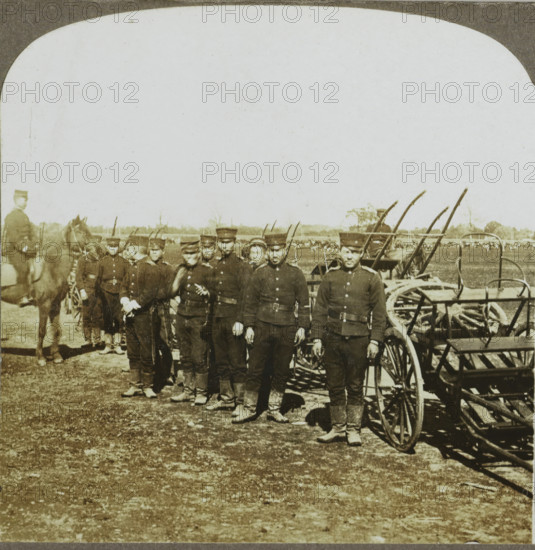 Artillery Wagons of First Division, Seoul, Korea, Korean soldiers for weaponry, stereograph, copyright notice: 'Copyright 1904, by George W. Griffith.', number: '1.', publisher: Griffith & Griffith, Philadelphia, 1904, photographer, North America, paper, pasteboard, baryta paper, gelatin silver print, developing gelatin silver print, height 89 mm x width 178 mm, the soldier, the soldier's life, (military) equipment and supply, A group of uniformed men stand in a line outdoors in front of horse-drawn equipment, each wearing dark jackets, caps, belts, and boots, with some holding items at their sides; a mounted man on a horse appears at one end of the line, several wheels and shafts of carts and equipment are visible behind and beside the men, and an open field with distant trees fills the background under a pale sky.