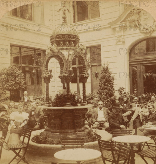 Waiting for their favorite Beverage, Cafe Linden, Berlin, Germany, Warten auf ihr Lieblingsgetränk, Deutschland, Terrace of Café Linden in Berlin, stereograph, inscription: 'Sold only by Underwood & Underwood, Liverpool, New-York, Chicago, Toronto, Ottawa, Kas.- El Paso, Tex.', inscription: 'Series 1894, by Bert Underwood.', inscription: '11', photographer: Bert Elias Underwood, publisher: Strohmeyer & Wyman, New York (city), 1894, North America, pasteboard, paper, albumen print, albumendruk, height 89 mm x width 178 mm, drinking, pavement, terrace in front of inn or restaurant, Unter den Linden, An ornate stone fountain with a domed decorative canopy stands in the center, surrounded by leafy plants and a circular basin, in front of a light-colored building facade with tall windows and an arched doorway; wooden chairs and round tables are arranged around the fountain, and a group of seated and standing people in period clothing, including men with hats and suits and a woman in a light-...