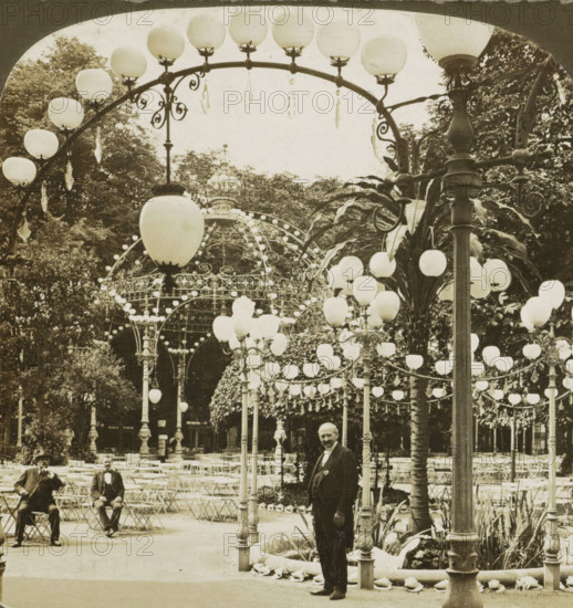 A scene in Kroll's Garden, -most famous beer garden in Berlin, Germany, Kroll's Biergarten in Berlin, stereograph, inscription: 'The ' PERFEC' STEREOGRAPH. (Trade Mark.), Patented April 14, 1903. Other Patents Pending.', copyright notice: 'Copyright 1902 by HC White Co.', number: '2102', inscription: 'A Scene in Kroll's Garden, Berlin, Germany., ', publisher: HC White Co., New York (city) (possibly), 1902, HC White Co., photographer, publisher, North America, New York (city), paper, pasteboard, gelatin silver print, developing gelatin silver print, height 88 mm x width 178 mm, pavement, terrace in front of inn or restaurant, A sepia-toned outdoor scene showing ornate arched metal frameworks adorned with numerous round globe lamps and hanging decorative elements, with a large domed metal structure in the background covered in light bulbs and scrollwork, rows of folding chairs and small round tables arranged beneath the arches, tall lamp posts with decorative bases and clusters of globe ...