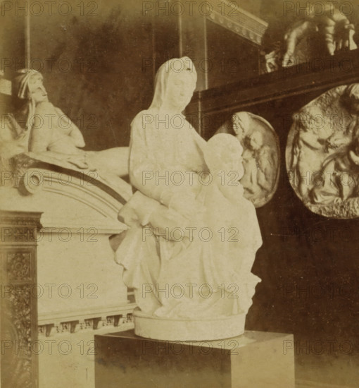 Neues Museum. Saal der Neuzeit. Maria mit dem Kinde von Michel Angelo, Madonna by Michelangelo in the Neues Museum, Berlin, Berlin und Umgebung, stereograph, inscription: 'Brügge, Liebfrauenkriche', number: '70.', photographer: Sophus Williams, after sculpture by Michelangelo, 1877, Michelangelo, after sculpture by, pasteboard, paper, albumen print, height 86 mm x width 176 mm, permanent exhibition, museum, monument, statue, Madonna: ie Mary with the Christ-child, Neues Museum, A pale stone sculpture of a seated veiled woman holding a child is centered on a pedestal, with draped folds of the woman's garment and the child's rounded head visible; to the left a reclining sculpted figure lies on an ornate curved base, and in the background there are circular relief panels with carved figures and a dark wooden ledge above them.