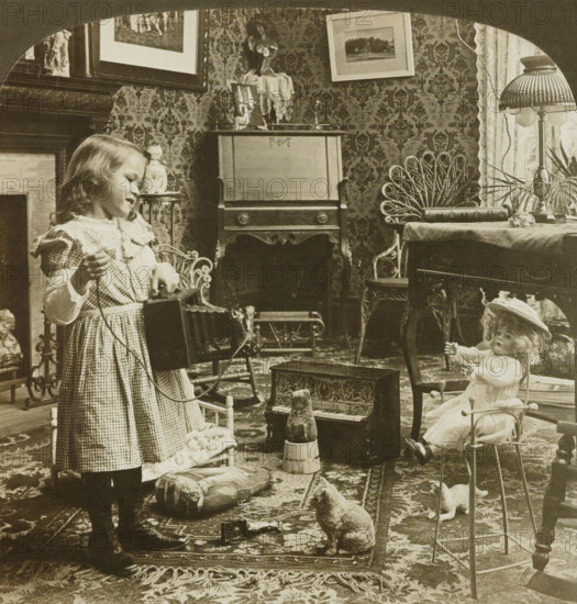 Now smile a little dolly while I take your picture, Girl takes a picture of her doll in a living room, stereograph, copyright notice: 'Copyright 1902 by HC White co.', inscription, number: '5213', inscription: 'The ' PERFEC' STEREOGRAPH. (Trade Mark.), Patented April 14, 1903. Other Patents Pending.', publisher: HC White Co., London (possibly), 1902, photographer, paper, pasteboard, gelatin silver print, developing gelatin silver print, height 89 mm x width 178 mm, girl (child between toddler and youth), (playing with) dolls, taking photographs, A young girl in a checked dress stands holding a cord and a small box, facing a room filled with furniture and toys; a doll sits in a small metal chair wearing a bonnet, another doll lies nearby, and a toy piano and a carved animal figure sit on a patterned rug. The room has ornate wallpaper, framed pictures on the wall, a wooden cabinet with decorative trim, a lamp with a fluted shade on a table draped with cloth, wicker chairs, cushions on th...
