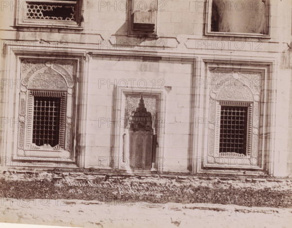 Brousse, niche et fenêtre de la Mosquée Verte, Façade of the Green Mosque in Bursa, photograph, number: 'No 70', photographer: Sébah & Joaillier, Bursa, 1888 - 1900, paper, albumen print, height 210 mm x width 268 mm, temple, shrine, Islam, Mohammedanism, Green Mosque, A section of a stone building facade with three framed recessed panels, two of the outer panels containing arched ornamental stonework and metal grilles, and a central recessed niche with a carved decorative fountain element; the stone surface shows weathering and stains, and the rectangular framing around each panel has raised molding; the lower edge of the image shows a rough stone ledge and textured ground.
