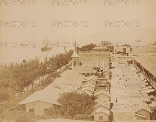 View of Port Tewfik, near the Suez Canal, Port Tewfik Suez, photograph, number: 'No. 138', inscription: 'Port Tewfik Suez, foto Zangaki', photographer: Zangaki, C. & G., Port Tewfik, 1870 - 1910, North Africa, Suez, pasteboard, paper, albumen print, albumendruk, height 219 mm x width 275 mm, height 348 mm x width 453 mm, city-view in general, 'veduta', canal, Suez Canal, A sepia-toned coastal scene showing a row of tiled-roof buildings and houses extending along a street toward the waterfront, with a church tower and steeple rising among the rooftops, trees lining a promenade beside the water, several sailing vessels and ships anchored or sailing on a calm sea, a few small figures walking in the street, and low-lying structures and vegetation along the shoreline.
