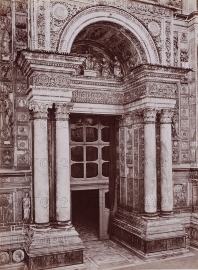 Porta della Chiesa, Portal of the monastery church Certosa di Pavia in Pavia, Italy, Certosa di Pavia, photograph, number: '13', inscription: 'Brogi (t)', number: '4621.', Pavia (city), publisher: attributed to Giacomo Brogi, Florence, 1856 - 1881, photographer, Tuscany, Lombardy, Attributed to, pasteboard, paper, albumen print, height 404 mm x width 306 mm, parts of church exterior and annexes: portal, A stone entrance framed by ornate carved columns and decorative pilasters with sculpted reliefs and medallions, an arched tympanum above filled with carved figures and painted panels, a deep recessed doorway with a paneled window above and a partially open curtain hanging to one side, carved capitals atop the columns, layered cornices with egg-and-dart and leaf motifs, patterned stone floor tiles at the threshold, and decorative friezes and sculpted figures integrated into the surrounding façade.