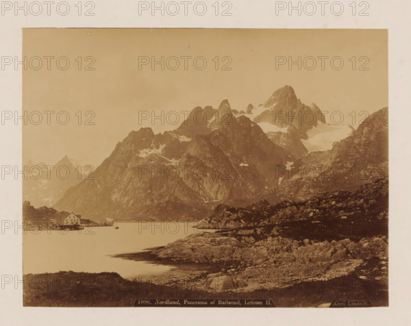 View of the Raftsundet near the Lofoten, Nordland, panorama from Raftsund, Lofoten, photograph, name: '1096.', photographer: Axel Lindahl, Raftsundet, 1883 - 1900, pasteboard, paper, albumen print, height 168 mm x width 220 mm, height 346 mm x width 456 mm, fjord, sea loch, A wide sepia-toned landscape shows steep rocky mountains with patches of snow rising behind a calm body of water, rocky shoreline in the foreground with textured boulders and sparse vegetation, a small pier with a wooden building on stilts at the water’s edge and a small boat moored nearby, distant peaks and ridgelines filling the middle and background under a pale sky.
