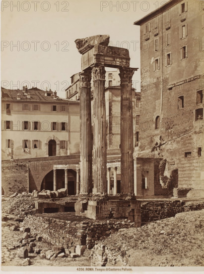 Tempio di Castore e Polluce, Remains of the Temple of Castor and Pollux in Rome, Italy, Roma, photograph, number: '4206.', inscription: 'Brogi (t), MB', number: '9', number: '57.', photographer: attributed to Giacomo Brogi, Rome, publisher: attributed to Edizioni Brogi, Florence, 1864 - 1881, Tuscany, Attributed to, pasteboard, paper, albumen print, height 375 mm x width 277 mm, ruin of a building, architecture, temple, shrine, Roman religion, Temple of Castor and Pollux (Rome), Three tall, fluted stone columns with ornate capitals stand on a stepped stone base among scattered blocks and rubble, a partially intact entablature resting atop them showing carved decorative elements and a fractured corner; behind the columns are multi-story buildings with shuttered windows and arched openings, textured brick and plaster facades, and a recessed colonnaded arcade visible through a large archway, while the foreground shows layered stone retaining walls and uneven ground strewn with broken maso...
