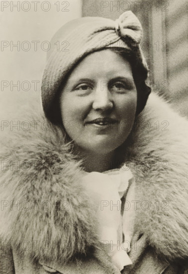 Portrait of Princess Juliana, photograph, picture postcard, London, publisher: Have, W. ten, Amsterdam, 1934, photographer, paper, gelatin silver print, developing gelatin silver print, height 153 mm x width 105 mm, Person, Juliana of the Netherlands, historical persons, crown princess, A close-up portrait of a woman wearing a cloche-style hat with a knot detail at the front and a large, fluffy fur collar around her neck; she has a slight smile, visible eyes and lips, and smooth facial features, with the background showing a softly textured, out-of-focus surface.