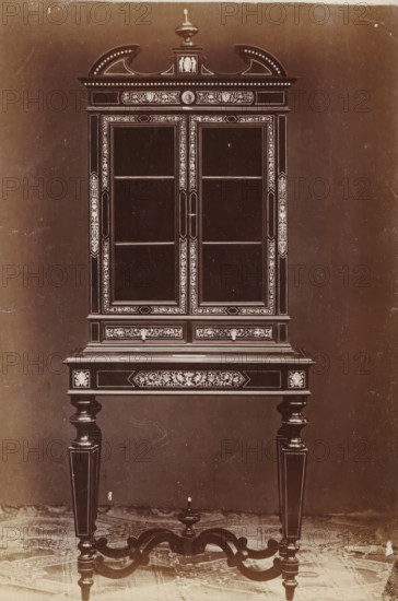 Secretaire, No 8 Mobile, photograph, page, inscription: 'Ies. 280', inscription: 'Alto, 191. Largo, 86. Fondo, 48.', c. 1878 - c. 1885, photographer, paper, albumen print, height 135 mm x width 95 mm, Photo on unnumbered page., writing-table, writing-desk, cupboard, A tall ornate wooden cabinet with glass-front double doors stands on turned legs connected by curved stretcher supports; the cabinet features a decorative top with a central finial and carved crest, inlaid floral and geometric border motifs around the door frames and drawer fronts, small drawer knobs beneath the glass doors, narrow shelves visible through the glass, and contrasting lighter decorative inlays along the edges and panels, all shown against a plain backdrop and a patterned floor under the legs.