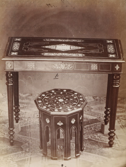 Table and stool with inlay, No 20 Tavola, Tambouret, photograph, page, number: '1., 2.', inscription: 'No 1. Ies. 180, ' 2 ' 45.', inscription: 'Alta, 76. Larga, 88. Fonda, 50., Alto 40. Largo 37.', c. 1878 - c. 1885, photographer, paper, albumen print, height 127 mm x width 95 mm, Photo on unnumbered page., table, stool, A close view of a wooden table with carved and inlaid decorative patterns on its flat top and apron, supported by turned, spiral legs, with a small octagonal wooden stool placed beneath it that has a patterned top and arched cutouts along its sides; a textured floor covering is visible under the furniture and the background above the table is plain and slightly mottled.