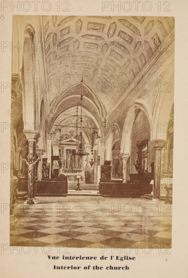 Photo reproduction of a drawing of the interior of the church of San Lazzaro degli Armeni, Venice, Vue intérieure de l'Eglise, Interior of the church, photograph, reproduction, page, number: '19B', after drawing by anonymous, c. 1874 - in or before 1879, photographer, after drawing by, paper, albumen print, height 128 mm x width 89 mm, Photo on unnumbered page opposite page 19., interior of church, San Lazzaro degli Armeni, A sepia-toned photograph of a large church interior showing a patterned floor with alternating light and dark tiles leading toward an elevated altar area framed by arches and columns, a vaulted ceiling decorated with recessed geometric panels, hanging chandeliers descending from the ceiling, ornate altar furnishings and statues positioned behind and around the altar, tall archways and columns lining the nave, a crucifix mounted on a stand near the foreground at one side, wooden pews and decorative architectural details along the side walls, and a wide aisle running ...