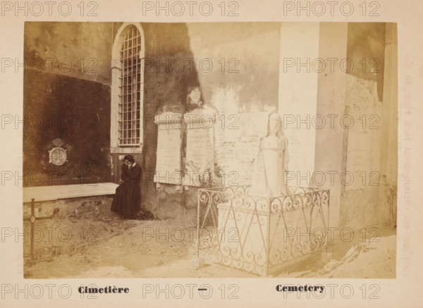 Cimetière - Cemetery, Cemetery of San Lazzaro degli Armeni, Venice, photograph, page, c. 1874 - in or before 1879, photographer, paper, albumen print, height 90 mm x width 130 mm, Photo on unnumbered page opposite page 25., churchyard, cemetery, San Lazzaro degli Armeni, A sepia photograph showing a courtyard area with aged stone walls and a tall arched window with metal bars, two upright stone grave markers mounted against the wall, a stone statue of a robed figure standing on a pedestal enclosed by an ornate metal railing, and a seated woman in dark clothing leaning against the wall with her face partially obscured by her hand.