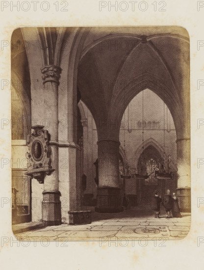 Photo reproduction of the painting 'In the Church in Haarlem' by Jan Jacob Schenkel, photograph, reproduction, page, photographer: Binger & Chits, after painting by Jan Jacob Schenkel, c. 1866 - in or before 1871, paper, albumen print, height 163 mm x width 137 mm, interior of church, Haarlem, A sepia-toned interior view of a vaulted stone building showing tall rounded columns and ribbed arches, with a decorative carved wall plaque mounted on one column, hanging chandeliers shaped like boats suspended from the ceiling, a tiled floor with visible stone seams and a circular decorative floor motif, and a small group of three people standing and conversing near one of the columns.