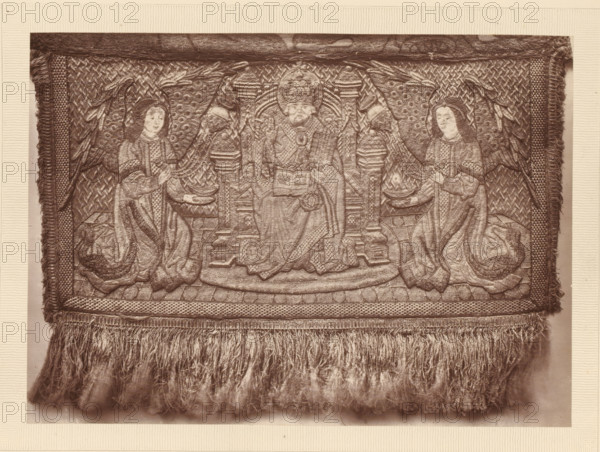 Part of an embroidered pall, A portion of a pall, page, photomechanical print, number: 'NO. 53.', inscription: 'Lent by the Fishmongers' Company', photographer: Isabel Agnes Cowper, United Kingdom, cliché maker: anonymous, after design by anonymous, c. 1869 - in or before 1874, Isabel Agnes Cowper, photographer, cliché maker, after design by, paper, Woodburytype, Woodburytypepie, height 148 mm x width 207 mm, (other forms of) needlework, eg: crocheting, knitting, embroidering, A rectangular woven textile panel with a fringed lower edge is shown; the panel features an ornate central scene with a seated figure wearing a tall rounded headdress and holding an open book, flanked by two kneeling figures in flowing robes and veiled heads, each holding shallow bowls and standing before decorative columns and patterned backgrounds; large stylized wings or feathered motifs extend behind the kneeling figures, and the panel is bordered by textured bands and tasselled edges with dense fringe hangin...