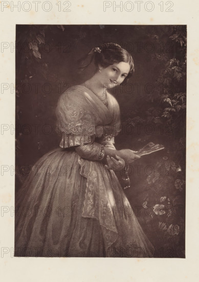 Photo reproduction of an engraving after the painting The beauty of Albano by August Riedel, reproduction, page, photomechanical print, photographer: Godfrey Wordsworth Turner, cliché maker: anonymous, after print by anonymous, after painting by August Riedel, c. 1866 - in or before 1871, after print by, paper, Woodburytype, Woodburytypepie, height 161 mm x width 118 mm, Print on second unnumbered page after page 58., adult woman, fan, print, eg: engraving, etching, lithograph, A sepia-toned portrait of a young woman wearing a full, floor-length dress with a fitted bodice and lace-trimmed shawl draped over her shoulders, her hair styled and adorned with a floral accessory and a ribbon, she holds a folding fan with both hands at waist level, jewelry including a necklace and earrings visible, a patterned sash and delicate lace details on her sleeves and skirt, foliage and flowers form a dark, textured background around her.