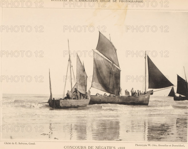 Fishing boats in the surf, De Panne, page, photomechanical print, inscription: 'Concours de négatifs 1888, Médaille de Bronze', photographer: Emile Solvyns, cliché maker: Wilhelm Otto, Brussels, c. 1883 - in or before 1888, printer (person), paper, collotype, photoprint, height 120 mm x width 169 mm, Print on unnumbered page., beach, sailing-ship, sailing-boat, sea (seascape), Several wooden sailboats sit in shallow water near the shore, their sails raised and catching a light breeze. The boats vary in size and shape, with tall masts and triangular sails in darker tones. Figures are visible on the boats, some standing and some seated, engaged in handling ropes and equipment. The water in front of the boats shows gentle waves and reflections of the hulls and sails. The scene is framed by a pale sky above and a narrow strip of shoreline at the bottom.