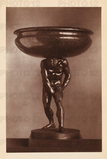 Porphyry bowl supported by a bronze statue of Hercules, from the collection of Christopher Beckett Denison, page, photomechanical print, number: '807', after sculpture by anonymous, c. 1880 - in or before 1885, after sculpture by, paper, Woodburytype, height 186 mm x width 122 mm, Print on seventh unnumbered page after page 78., (story of) Hercules (Heracles), dish, plate, saucer, piece of sculpture (precious metals, arts), A sepia photograph of a sculpture showing a muscular male figure standing on a round stepped base, the figure slightly bent forward with head lowered and one arm across the groin while the other grasps the wrist, supporting a large shallow bowl balanced on the back of the neck and shoulders; the bowl has a speckled surface and a rounded rim, the figure is detailed with defined musculature and textured hair, and the background is plain with a light-to-dark gradient.