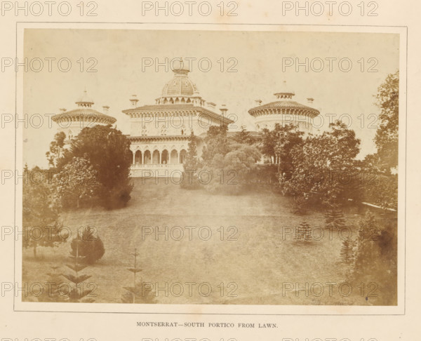 View of a portico of the Palácio de Monserrate near Sintra, Montserrat - South portico from lawn, photograph, page, Sintra, c. 1865 - in or before 1870, photographer, paper, albumen print, height 143 mm x width 197 mm, palace, gate, entrance, Palácio de Monserrate, A sepia-toned photograph showing a large ornate building with a central dome and two round towers on either side, all topped with decorative roofs and small cupolas, a portico with a row of arched openings across the front, balustrades beneath the arches, and carved architectural details along the cornices; the building is set behind a gently sloping grassy lawn bordered by dense trees and shrubs of varying heights that partially obscure the lower façade, with scattered small plantings visible on the lawn and a pale sky above.
