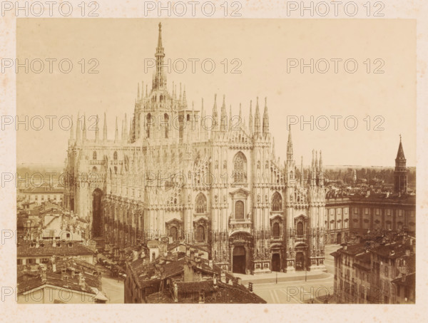 View of the Milan Cathedral, photograph, signature: 'Fotografia Artistica P. Pozzi Milano', photographer: Pompeo Pozzi, publisher: William Spooner, c. 1860 - c. 1865, pasteboard, paper, albumen print, height 256 mm x width 358 mm, Lombardy, Milan, Cathedral (Milan), A wide sepia-toned view of an ornate Gothic cathedral facade dominated by tall spires, pointed arches, intricate tracery, and carved statues, with detailed doorways and large stained glass window openings; surrounding the cathedral are densely packed old buildings with tiled roofs and narrow streets, and a square in front of the cathedral with a paved surface; in the distance a tall tower with a conical roof rises above lower rooftops, and the sky above is pale and mostly clear.