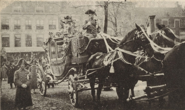 The golden coach of the wedding procession of Wilhelmina, Queen of the Netherlands, and Hendrik of Mecklenburg-Schwerin in The Hague on February 7, 1901, postcard, photomechanical print, The golden coach of the wedding procession of Wilhelmina and Hendrik in The Hague on February 7, 1901. In the right margin a line of Dutch text., inscription, clichémaker: anonymous, Netherlands, photographer, paper, collotype, photogravure, height 90 mm x width 142 mm, The title mentioned here refers to the highest title obtained by the person portrayed, not necessarily to the title the person portrayed bears in this image., Person, Hendrik (Prince of the Netherlands (1876-1934)), Wilhelmina of the Netherlands, (civil) marriage ceremonies, animal traction, animal-drawn vehicle (carriage etc.), Marriage of Queen Wilhelmina and Prince Hendrik, The Hague, Period, 1901-02-07, A sepia-toned street scene showing an ornate, horse-drawn carriage with decorative trim and carved details, draped fabric on its si...