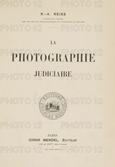 La photographie judiciaire, book, name: 'Reinders', writer (clerical worker): Rodolphe Archibald Reiss, publisher: Charles Mendel, Paris, 1903, writer (clerical worker), textile materials, pasteboard, paper, linen (material), printing, marbled paper, gelatin silver print, autotype, developing gelatin silver print, height 248 mm x width 185 mm x thickness 25 mm, A vertical cream-colored page with centered dark serif headings and a circular emblem lower on the page; the top shows a small bold heading, beneath it narrower lines of smaller text, then a thin horizontal rule, followed by a single short word in medium-sized serif; below that a large bold word in wide spaced capital letters followed by another medium bold word; lower on the page is a round decorative seal with an inner illustration and concentric patterned border; near the bottom are additional lines of smaller serif text and a small centered short line above the very bottom of the page.