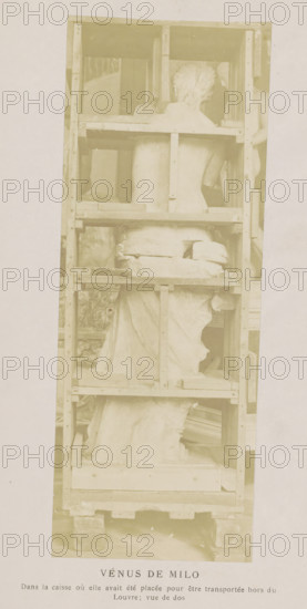 Venus de Milo in a transport box, seen from the back, Vénus de Milo, photograph, page, inscription: 'Dans la caisse, vue de dos', c. 1861 - in or before 1871, photographer, paper, albumen print, height 179 mm x width 67 mm, sculpture, (story of) Venus (Aphrodite), A tall wooden crate with horizontal and vertical planks holds a fragmented marble statue shown from the back, with a torso and draped lower body visible, the statue’s head turned slightly to one side and supported within the crate, and wooden blocks and padding placed around the sculpture; the crate rests on a pallet and the photograph has a light, faded tone.