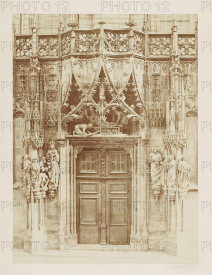 Entrance portal of the Saint Lawrence Chapel of the Strasbourg Cathedral, photograph, page, photographer: Charles David Winter, Strasbourg (France), c. 1851 - in or before 1861, paper, albumen print, height 148 mm x width 110 mm, sculpture (relief, sculpture), parts of church exterior and annexes: portal, Notre-Dame (Strasbourg), A tall ornate doorway set into a stone façade with carved panels and a central wooden double door framed by decorative molding, above which sits an elaborate canopy of pointed arches and foliated tracery with sculpted figures and relief work; flanking the entrance are clustered vertical columns with pinnacles and niches containing statues of robed figures standing on small plinths, and additional carved architectural ornamentation fills the upper facade with repeating quatrefoil patterns and intricate stone latticework.
