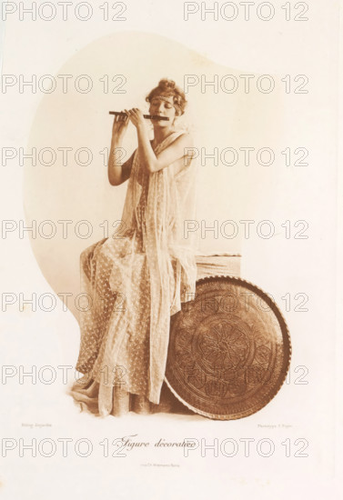 Figure décorative, Woman playing flute with a bowl, page, photomechanical print, photographer: Constant Puyo, France, cliché maker: Paul Dujardin, printer (person): Charles Wittmann, Paris, c. 1886 - in or before 1896, printer (person), paper, photoaquatint, height 211 mm x width 144 mm, transverse flute, adult woman, serving-dish, platter, A sepia-toned portrait of a seated woman wearing a sheer, patterned draped gown and a decorative headband, holding a flute to her lips with both hands and eyes closed, positioned beside a large round ornate tray with embossed geometric and floral designs.