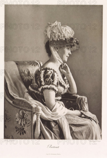 Portrait, Portrait of an unknown woman with a hat in a chair, page, photomechanical print, photographer: Constant Puyo, France, cliché maker: Paul Dujardin, printer (person): Charles Wittmann, Paris, c. 1886 - in or before 1896, printer (person), paper, photoaquatint, height 211 mm x width 153 mm, adult woman, head-gear: hat, chair, A sepia-toned portrait of a seated woman in profile facing right, wearing a large ornate bonnet with ruffled fabric and lace, a ribbon tied beneath her chin, and a dress with puffed sleeves trimmed with ruffles; she rests one hand lightly against her neck and her other hand lies in her lap, while she sits on a patterned upholstered chair draped with fabric and a long flowing skirt cascades over the seat and armrest.