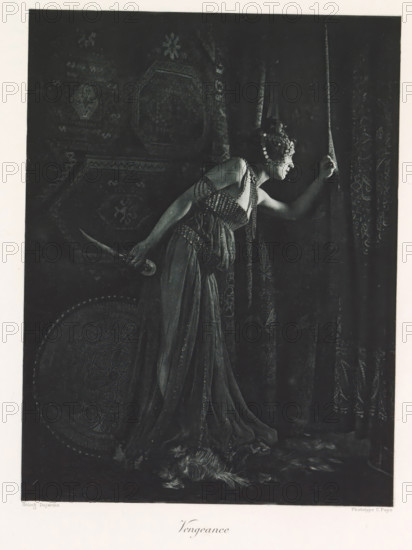 Woman with a knife in hand, depicting the Revenge, Vengeance, page, photomechanical print, photographer: Constant Puyo, France, cliché maker: Paul Dujardin, printer (person): Charles Wittmann, Paris, c. 1886 - in or before 1896, printer (person), paper, photoaquatint, height 216 mm x width 164 mm, adult woman, curtains, tools, aids, implements, crafts and industries: knife, A monochrome image shows a woman in a flowing dress leaning forward and parting a heavy patterned curtain with one hand while holding a curved dagger behind her back with the other; she wears an ornate headpiece with round decorative elements and beaded straps across her shoulders and bodice, and a round decorated shield rests near her side while a feathered object lies on the floor at her feet.